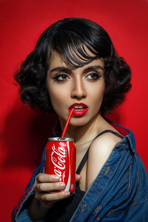 Model trinkt Coca-Cola vor rotem Hintergrund